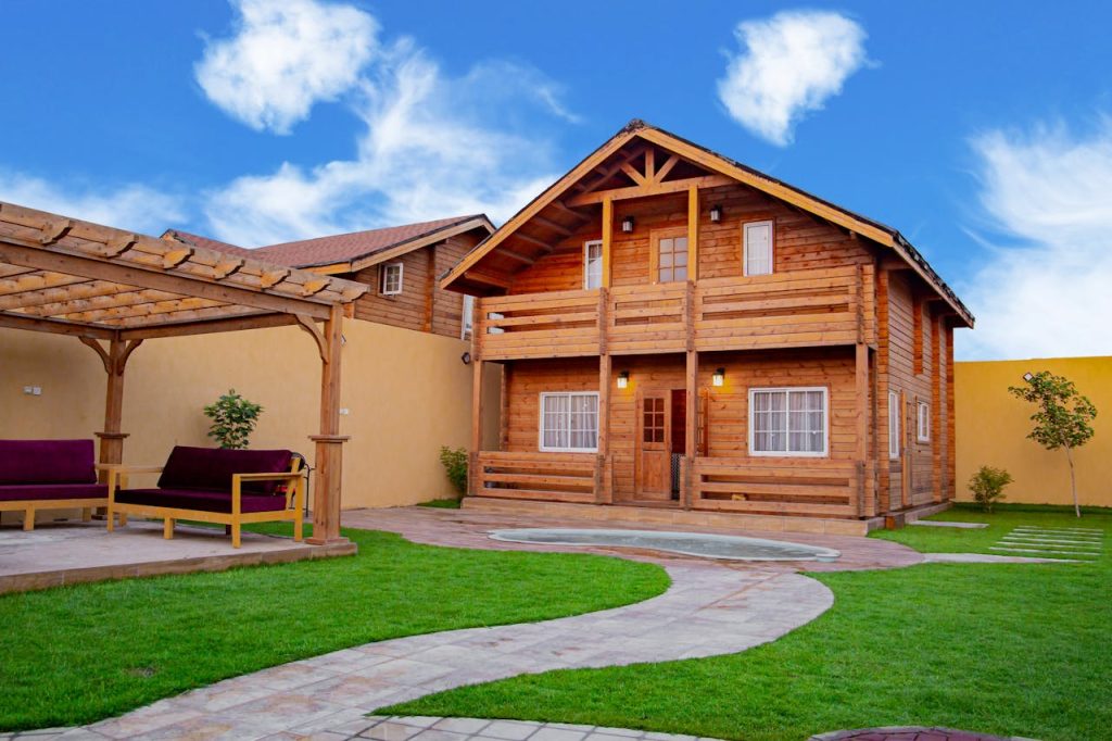 Rustic wooden house with a patio and well-maintained lawn under a vibrant blue sky.