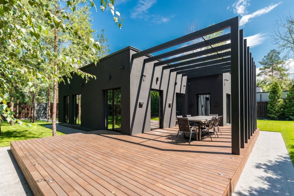 terrace-in-house-7587879 Stylish outdoor space with wooden deck and dining set, surrounded by lush greenery.